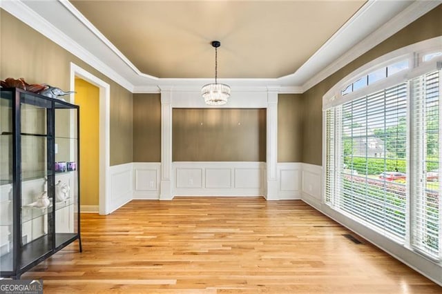 205 Camden Creek Ct, Lawrenceville, GA 30043 - unfurnished dining area featuring a chandelier, light wood-type flooring, a raised ceiling, a decorative wall, and ornate columns