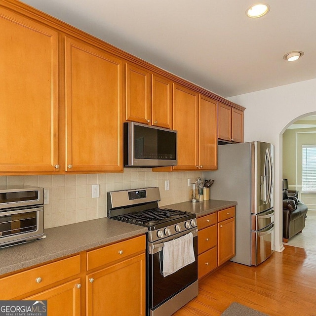 3439 Tupelo Trl, Auburn, GA 30011 - kitchen featuring stainless steel appliances, arched walkways, light wood-style floors, brown cabinetry, and dark countertops