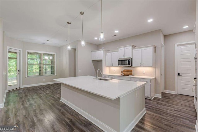 150 Whitworth Dr, Locust Grove, GA 30248 - kitchen with stainless steel microwave, white cabinets, dark wood-style floors, backsplash, and a center island with sink