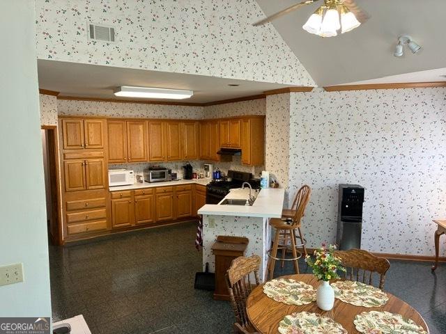 9361 Arbor Glenn Ct, Jonesboro, GA 30263 - kitchen with wallpapered walls, white microwave, black range with gas cooktop, light countertops, and a peninsula