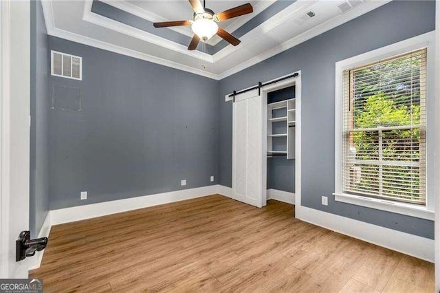 908 Basingstoke Ct, Suwanee, GA 30024 - unfurnished bedroom featuring ornamental molding, multiple windows, a raised ceiling, light wood finished floors, and a barn door