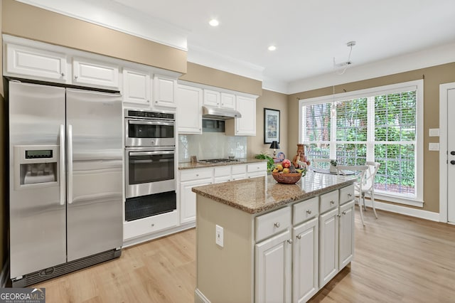 1065 Bookhout Dr, Cumming, GA 30041 - kitchen featuring appliances with stainless steel finishes, light wood-type flooring, a kitchen island, tasteful backsplash, and light stone counters