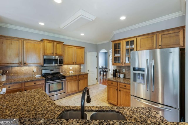 168 Gatlin Ridge Run, Dallas, GA 30157 - kitchen featuring appliances with stainless steel finishes, brown cabinetry, arched walkways, decorative backsplash, and glass insert cabinets