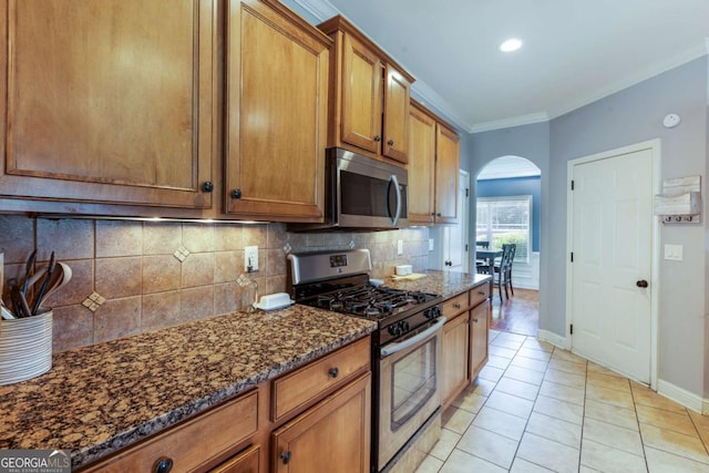 168 Gatlin Ridge Run, Dallas, GA 30157 - kitchen with appliances with stainless steel finishes, arched walkways, brown cabinetry, decorative backsplash, and dark stone counters