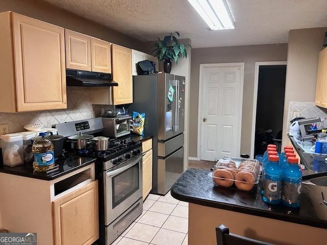 8519 Glenwoods Dr, Riverdale, GA 30274 - kitchen featuring appliances with stainless steel finishes, under cabinet range hood, dark countertops, decorative backsplash, and light brown cabinets