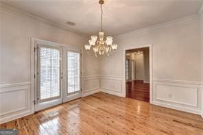 2324 Blackberry Ct, Snellville, GA 30078 - unfurnished dining area featuring a chandelier, a decorative wall, ornamental molding, wood finished floors, and a wainscoted wall