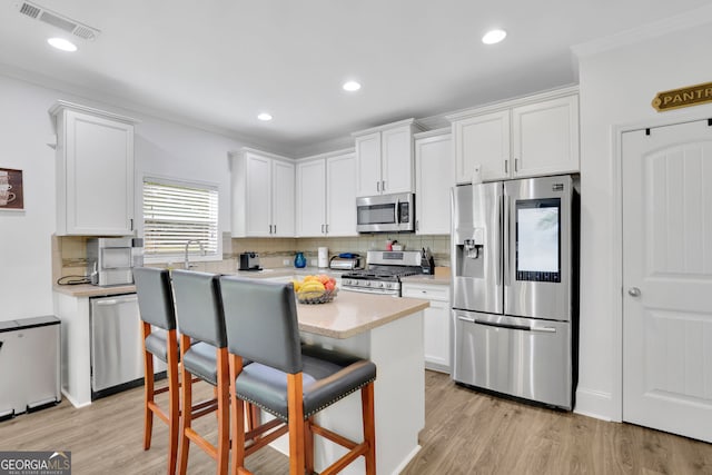425 Eldridge Dr, Suwanee, GA 30024 - kitchen with appliances with stainless steel finishes, decorative backsplash, white cabinets, ornamental molding, and a kitchen bar