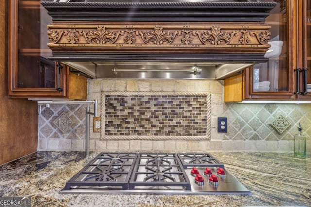 3887 Hickory Manor Dr, Suwanee, GA 30024 - kitchen featuring stainless steel gas stovetop, glass insert cabinets, decorative backsplash, extractor fan, and stone counters