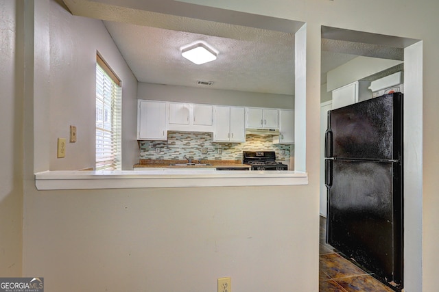 5026 Brittany Dr, Stone Mountain, GA 30083 - kitchen with black appliances, under cabinet range hood, white cabinetry, a textured ceiling, and backsplash
