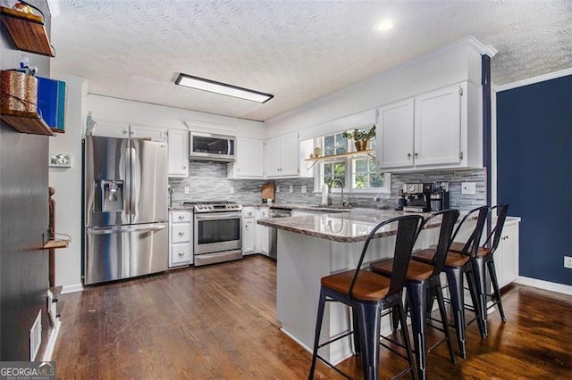 1452 Crooked Tree Cir, Stone Mountain, GA 30088 - kitchen with appliances with stainless steel finishes, a peninsula, a textured ceiling, backsplash, and white cabinetry