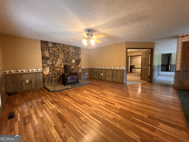 172 Fred Henry Ln, Clayton, GA 30525 - unfurnished living room with wood finished floors, wainscoting, a wood stove, a textured ceiling, and a ceiling fan