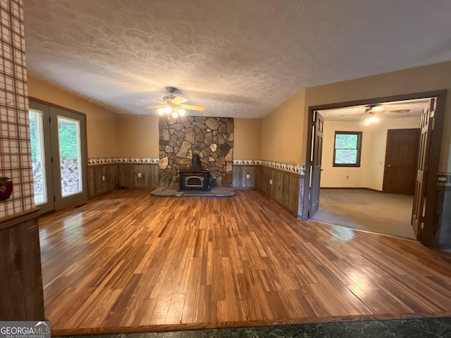 172 Fred Henry Ln, Clayton, GA 30525 - unfurnished living room featuring a ceiling fan, hardwood / wood-style floors, a wainscoted wall, a textured ceiling, and a wood stove