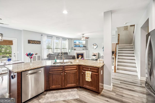 2755 Evan Manor Ln, Cumming, GA 30041 - kitchen featuring appliances with stainless steel finishes, ceiling fan, light wood-style floors, a lit fireplace, and open floor plan