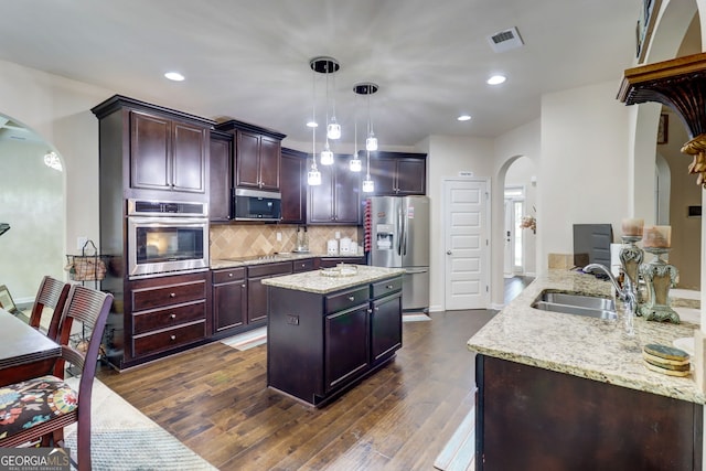 312 Sierra Ct, Mcdonough, GA 30253 - kitchen featuring appliances with stainless steel finishes, arched walkways, light stone counters, decorative backsplash, and dark wood-type flooring