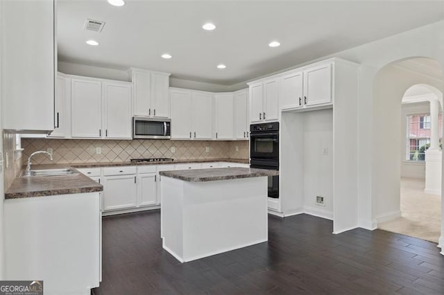 3366 Bridge Walk Dr, Lawrenceville, GA 30044 - kitchen with stainless steel microwave, dark countertops, arched walkways, dark wood-style floors, and backsplash