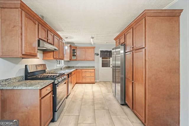 4212 Worth St NW, Acworth, GA 30101 - kitchen featuring appliances with stainless steel finishes, under cabinet range hood, a textured ceiling, light stone counters, and glass insert cabinets