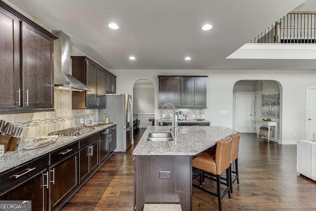 1830 Secretariat Gait Way, Suwanee, GA 30024 - kitchen with wall chimney range hood, stainless steel appliances, arched walkways, light stone counters, and dark wood finished floors