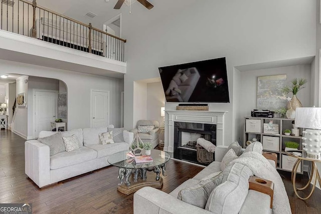 1830 Secretariat Gait Way, Suwanee, GA 30024 - living room featuring a ceiling fan, a towering ceiling, arched walkways, a premium fireplace, and wood finished floors