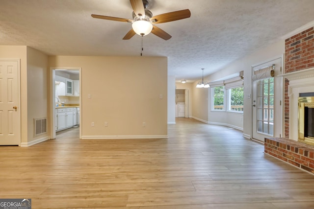 120 Fox Hunt Pl, Athens, GA 30606 - unfurnished living room featuring a textured ceiling, a brick fireplace, light wood-style flooring, ceiling fan, and a chandelier