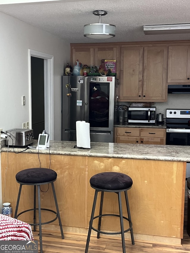 17 Dime St, Douglas, GA 31535 - kitchen featuring appliances with stainless steel finishes, extractor fan, a textured ceiling, light wood finished floors, and a breakfast bar area