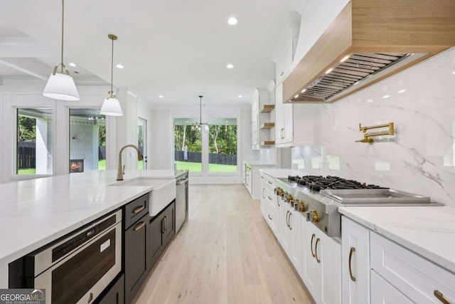3205 Bold Springs Rd, Dacula, GA 30019 - kitchen with ventilation hood, white cabinetry, light wood finished floors, stainless steel appliances, and pendant lighting
