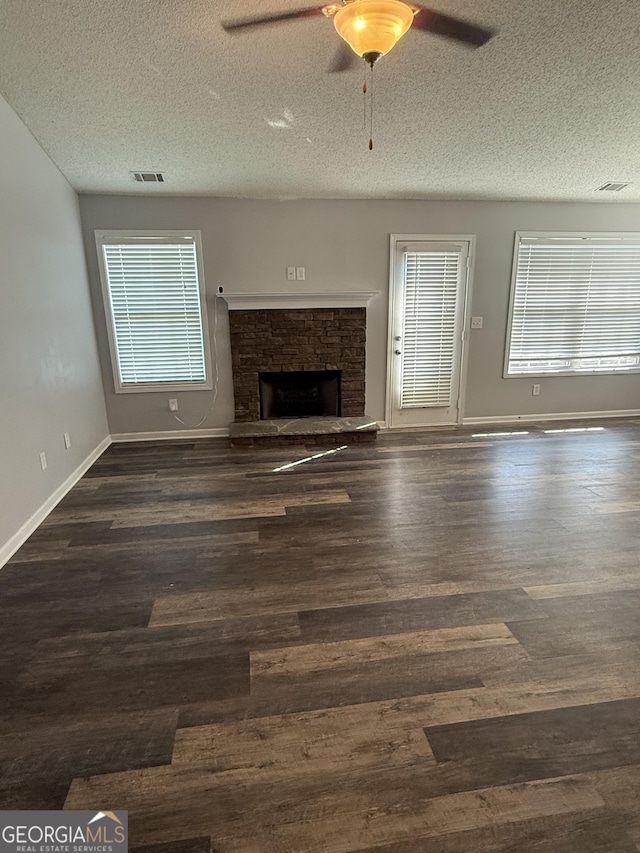 330 Anchors Way, Winder, GA 30680 - unfurnished living room featuring a textured ceiling, a stone fireplace, a ceiling fan, and dark wood-style floors