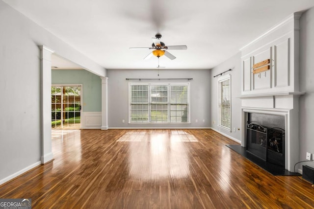 5035 Foxberry Ln, Roswell, GA 30075 - unfurnished living room with a fireplace with raised hearth, a ceiling fan, wood finished floors, and decorative columns