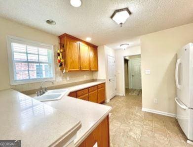 121 Pinnacle Ln, Mcdonough, GA 30253 - kitchen featuring freestanding refrigerator, brown cabinetry, a textured ceiling, and light countertops