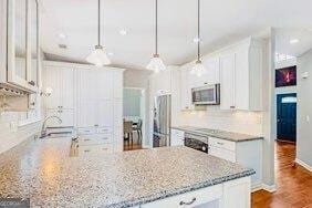 380 Victorian Ln, Duluth, GA 30097 - kitchen featuring stainless steel microwave, white cabinets, light stone countertops, hanging light fixtures, and decorative backsplash
