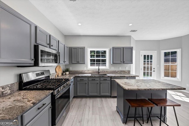 5195 Oaks Landing Ct, Sugar Hill, GA 30518 - kitchen featuring stainless steel appliances, gray cabinetry, a kitchen bar, light wood-style floors, and recessed lighting