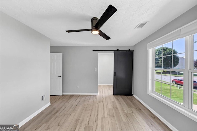 5195 Oaks Landing Ct, Sugar Hill, GA 30518 - unfurnished bedroom with a barn door, light wood-type flooring, a ceiling fan, and a textured ceiling