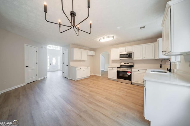 4815 Price St, Forest Park, GA 30297 - kitchen with stainless steel appliances, a chandelier, arched walkways, light wood-type flooring, and white cabinets