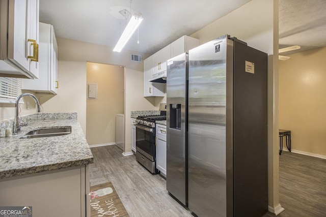 1077 Mainstreet Valley Dr, Stone Mountain, GA 30088 - kitchen with appliances with stainless steel finishes, under cabinet range hood, light wood-style flooring, white cabinets, and light stone countertops