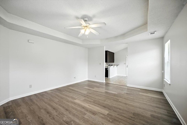 4801 Wilson Rd, Macon, GA 31206 - unfurnished living room with a tray ceiling, a ceiling fan, dark wood-style floors, and a textured ceiling