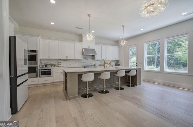 841 Keystone Dr, Woodstock, GA 30188 - kitchen featuring appliances with stainless steel finishes, under cabinet range hood, a chandelier, light wood-style flooring, and white cabinets