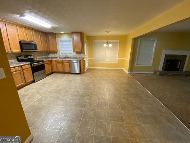 1472 Queenie Smith Rd NE, Conyers, GA 30012 - kitchen featuring appliances with stainless steel finishes, open floor plan, a chandelier, a fireplace with raised hearth, and brown cabinetry