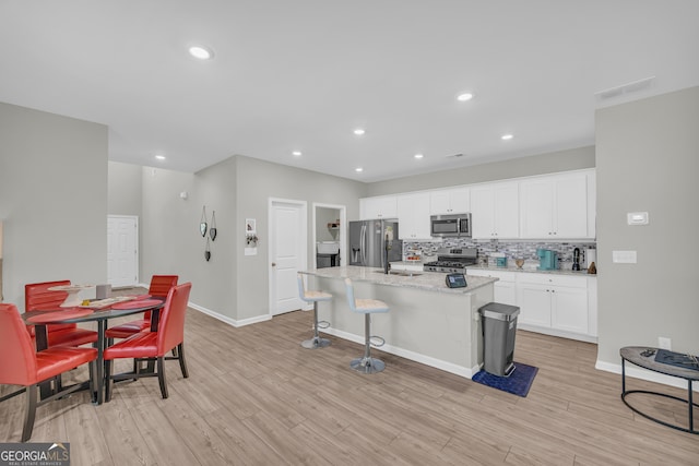 264 Golden Eagle Pkwy, Braselton, GA 30517 - kitchen with stainless steel appliances, a kitchen island, backsplash, white cabinetry, and light wood-style floors