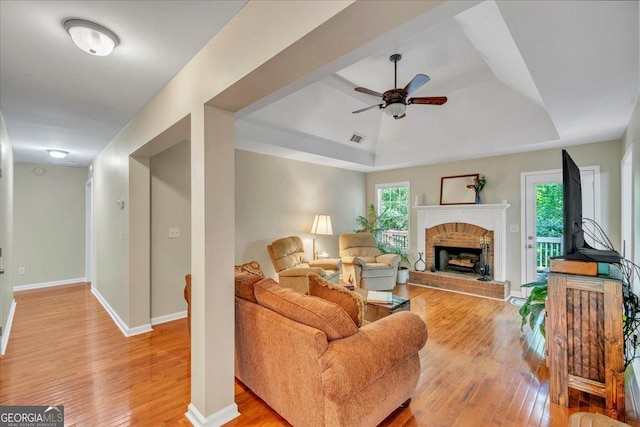 536 Sam Brown Blvd, Commerce, GA 30529 - living room featuring light wood finished floors, a ceiling fan, a brick fireplace, and a tray ceiling