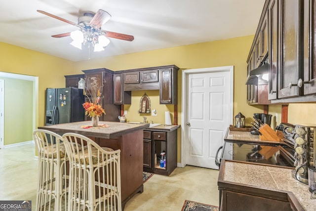 7769 Copper Kettle Way, Flowery Branch, GA 30542 - kitchen with dark brown cabinets, under cabinet range hood, black fridge with ice dispenser, and a ceiling fan
