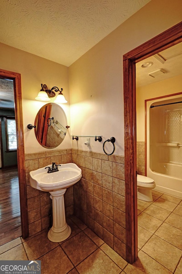 4393 Cannon Rd, Loganville, GA 30052 - full bathroom featuring tile walls, a wainscoted wall, tile patterned flooring, a textured ceiling, and shower / bathtub combination