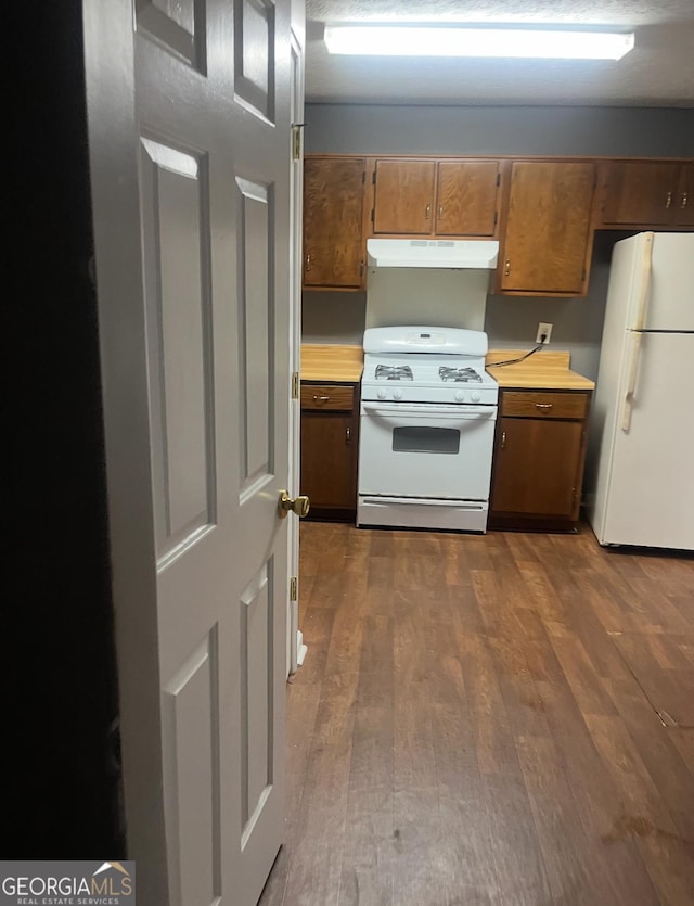 6470 Bedford Ln, Lithonia, GA 30058 - kitchen with white appliances, under cabinet range hood, light countertops, dark wood finished floors, and brown cabinetry
