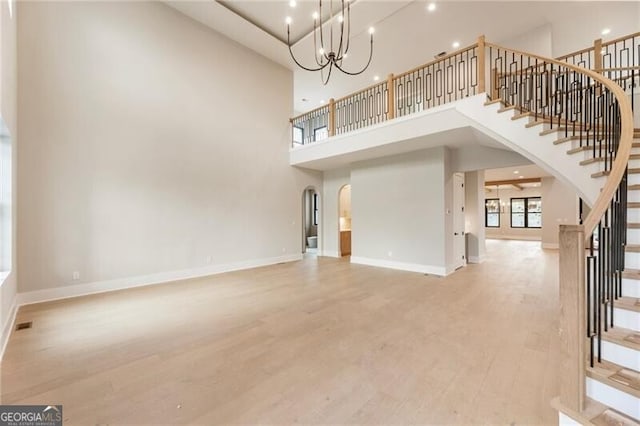 15792 Thompson Rd, Milton, GA 30004 - unfurnished living room with arched walkways, a high ceiling, light wood finished floors, stairs, and a chandelier