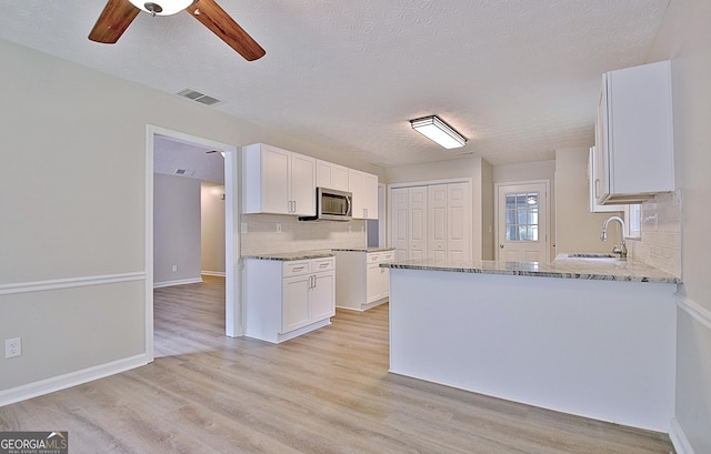 85 Holly Springs Rd, Sharpsburg, GA 30277 - kitchen with stainless steel microwave, tasteful backsplash, light stone countertops, white cabinets, and a textured ceiling