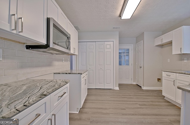 85 Holly Springs Rd, Sharpsburg, GA 30277 - kitchen featuring stainless steel microwave, light stone counters, white cabinetry, light wood-style flooring, and a textured ceiling