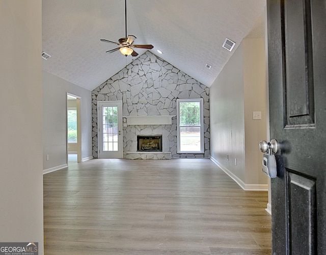 85 Holly Springs Rd, Sharpsburg, GA 30277 - unfurnished living room featuring a ceiling fan, healthy amount of natural light, vaulted ceiling, a stone fireplace, and light wood-style floors