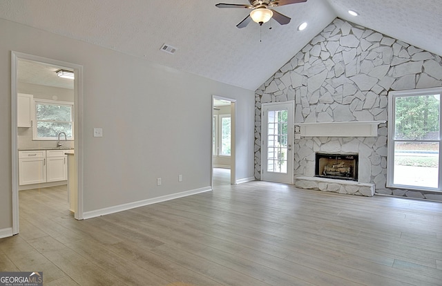 85 Holly Springs Rd, Sharpsburg, GA 30277 - unfurnished living room featuring ceiling fan, light wood finished floors, a stone fireplace, a textured ceiling, and high vaulted ceiling