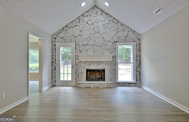 85 Holly Springs Rd, Sharpsburg, GA 30277 - unfurnished living room with lofted ceiling, a textured ceiling, wood finished floors, plenty of natural light, and a stone fireplace