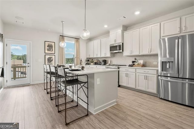 402 Nix Ln, Lawrenceville, GA 30046 - kitchen with stainless steel appliances, a kitchen island with sink, light countertops, backsplash, and light wood-type flooring