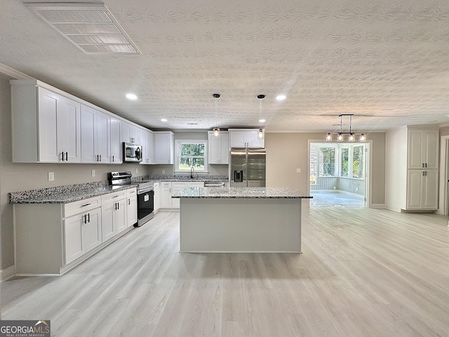 115 Creekside Ln, Covington, GA 30016 - kitchen with stainless steel appliances, light wood-type flooring, white cabinets, dark stone countertops, and a center island