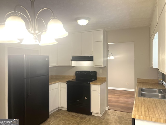 4263 Southvale Dr, Decatur, GA 30034 - kitchen with freestanding refrigerator, black range with electric cooktop, under cabinet range hood, white cabinetry, and a chandelier